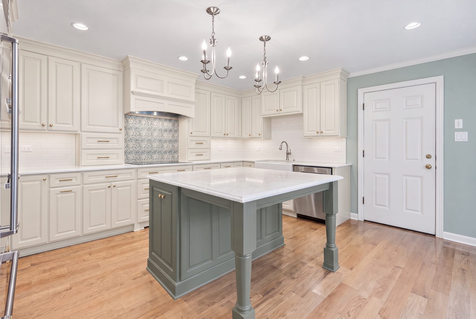 After: the same cabinets refinished in soft cream with a sage-grey island and brass hardware